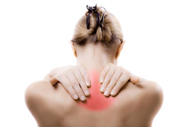 Back view of blond faceless lady in casual t shirt and manicure demonstrating pain spot on back while sitting near white wall
